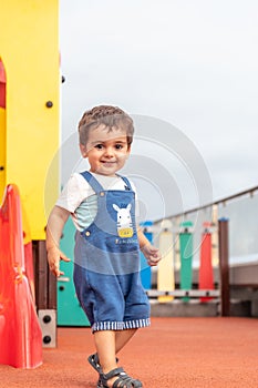 Vertical shot of a little boy having fun and running around on colorful playground equipment