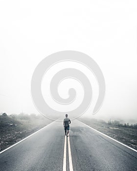 Vertical shot of a lonely male walking the road disappearing in a fog