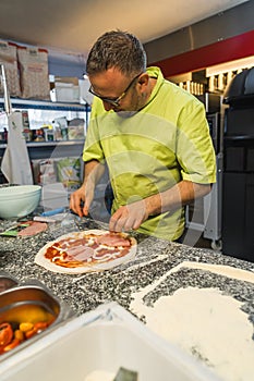vertical shot of a man cook adding meat and seasonings to prepare pizza