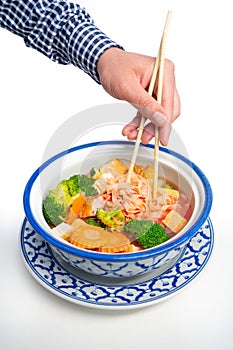 Vertical shot of a man holding chopsticks in a Thai Tofu Veggie dish in a traditional Thai bowl