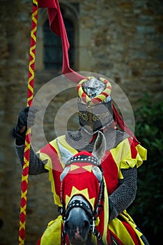 Vertical shot of a man on a horse in armor and with a spear with an old building in the background