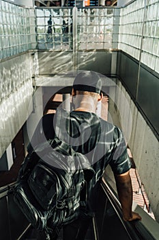 Vertical shot of a man photographed from behind going down the escalator with rays of sunlight on