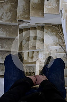 Vertical shot of a man sitting in the ruined staircase of an abandoned building