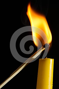 Vertical shot of a match lighting a candle isolated on a black background