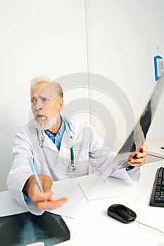 Vertical shot of mature adult male doctor explaining results of MRI scanning, giving professional consultation for