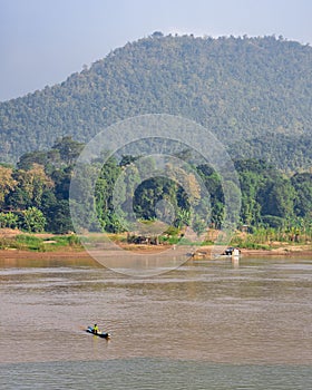 Vertical shot of the Mekong River with a floating boat near mountains in Luang Prabang, Laos