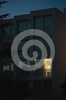 Vertical shot of a modern white building with light coming out from one of the big balcony windows