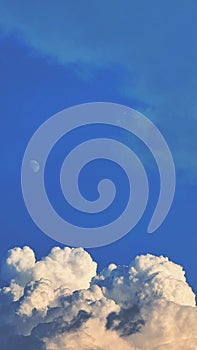 Vertical shot of the Moon against a cloudy bright blue sky perfect for wallpapers