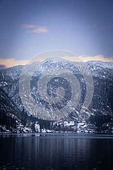 Vertical shot of a mountain range covered with snow against a lake on a cloudy day in winter