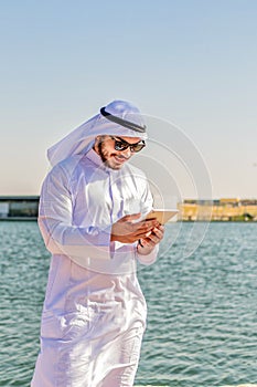Vertical shot of a Muslim male, in traditional clothes, checking content on a tablet
