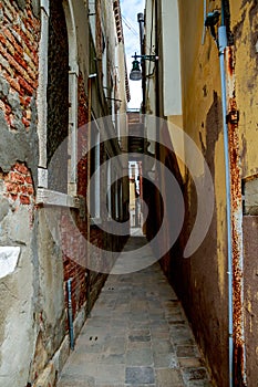 Vertical shot of a really narrow alley with old brickwalls on the sides in Venice, Italy