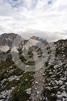 Vertical shot of a narrow path in the rocky cliff with the Passo Falzarego seen behind it