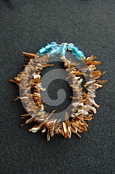 Vertical shot of a necklace made of brown puka shells and blue beads on a gray surface