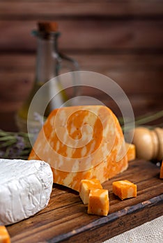 Vertical shot of Neuchatel and Colby orange cheese on a wooden board with herbs in the background