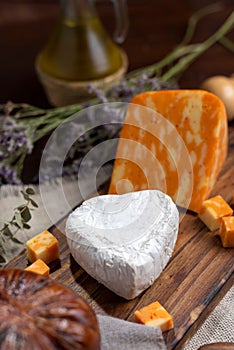 Vertical shot of Neuchatel and Colby orange cheese on a wooden board with herbs in the background