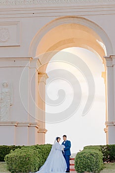 Vertical shot of a newly-wed couple posing outdoors in front of an arch