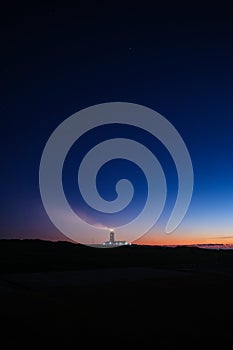 Vertical shot of the night over the silhouette of the land and a lighthouse in the background