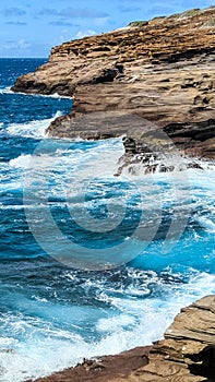 Vertical shot of the ocean waves crashing on the cliffs in Lanai Lookout, Oahu, Hawaii