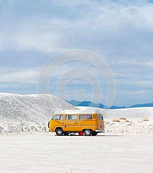 Vertical shot of an old orange van on snow-covered sand dunes