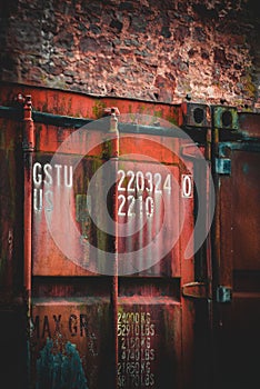 Vertical shot of old red rusty shipping container door with technical characteristics text