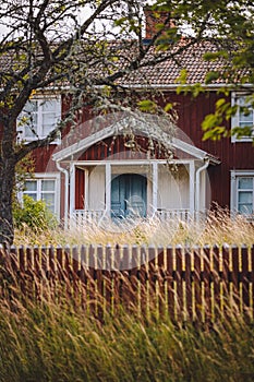 Vertical shot of an old red wooden house facade surrounded by trees and grass