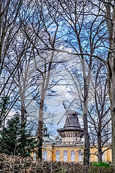 Vertical shot of an old windmill and tall wooden bare trees in daylight in Postdam garden, Berlin