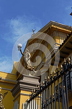 Vertical shot of an old yellow building with a black metal fence and decorated by sculptures