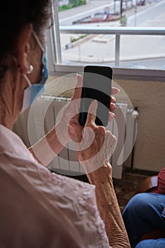 Vertical shot of an older woman wearing a facemask contacting her family via the smartphone