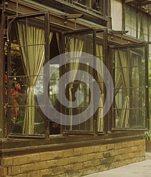 Vertical shot of open glass windows with tied curtains on a stone wall