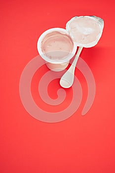 Vertical shot of an opened plastic container of fruit yogurt and a spoon, on a red surface