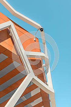 Vertical shot outdoor round CCTV camera on roof of building against blue sky.