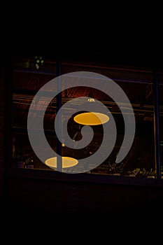 Vertical shot of a pair of yellow ceiling lights behind a window at night