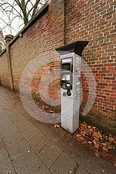 Vertical shot of a parking meter on a street before a red brick wall in a town
