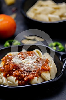 Vertical shot of a pasta dish, surrounded with ingredients on a black surface