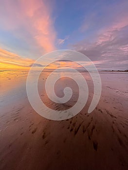 Vertical shot of a peaceful sunset at Morecambe Bay with sand visible in the transparent water