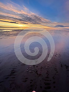 Vertical shot of a peaceful sunset at Morecambe Bay with sand visible in the transparent water