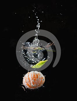 Vertical shot of peeled tangerine submerged in water isolated on black background