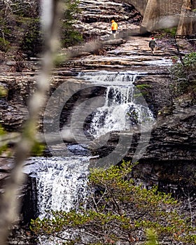 Vertical shot of people hiking above cliffs of large waterfall