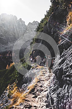 Vertical shot of people walking on the side of the mountain at daytime shot from behind