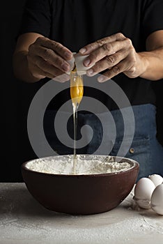 Vertical shot of a person dropping an egg into the bowl with flour