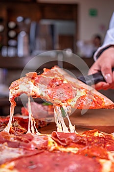 Vertical shot of a person holding a slice of pizza with a black tool