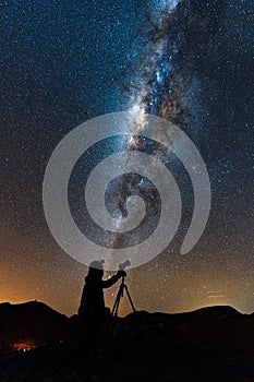 Vertical shot of a person in shadow with a telescope looking at starry sky