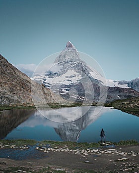 Vertical shot of a person standing by the Riffelsee Lake in the Matterhorn mountains in Switzerland