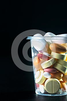 Vertical shot of pharmaceuticals pills and antibiotics in a plastic cup on a black background