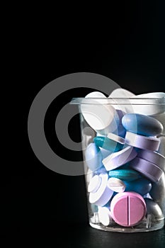 Vertical shot of pharmaceuticals pills and antibiotics in a plastic cup on a black background