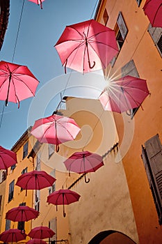 Vertical shot of pink umbrellas hanging above a street in a Grasse, France