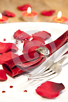 Vertical shot of a plate with red rose petals on a festive table with lit candles on a background