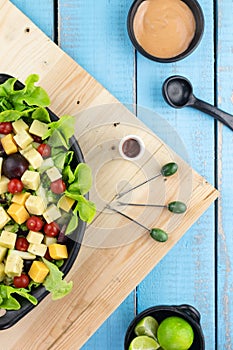 Vertical shot of a platter of fresh salad on a wooden table with food pickers