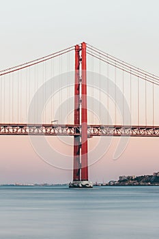 Vertical shot of Ponte 25 de Abril bridge in Lisbon, Portugal, with a sunset in the background