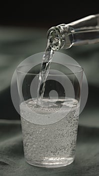 vertical shot pour tonic water in tumbler glass on linen cloth